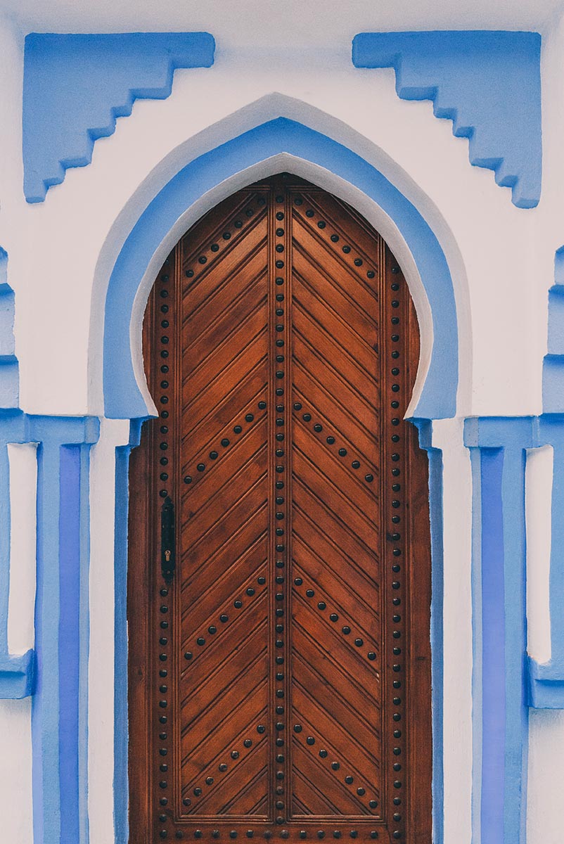 Malebné vstupní dřevěné dveře, rámované modrými oblouky, do jednoho z domů v městě Chefchaouen.